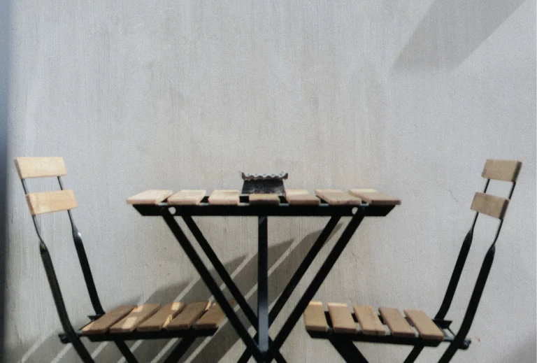 A minimalist outdoor table with two wooden chairs, ideal for a peaceful breakfast or relaxing time. The table is complemented by a simple decor piece, creating a cozy atmosphere.