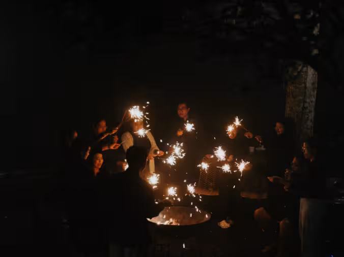 A group of people enjoying sparklers and a bonfire at Rimbun Farm, creating a warm and festive atmosphere.